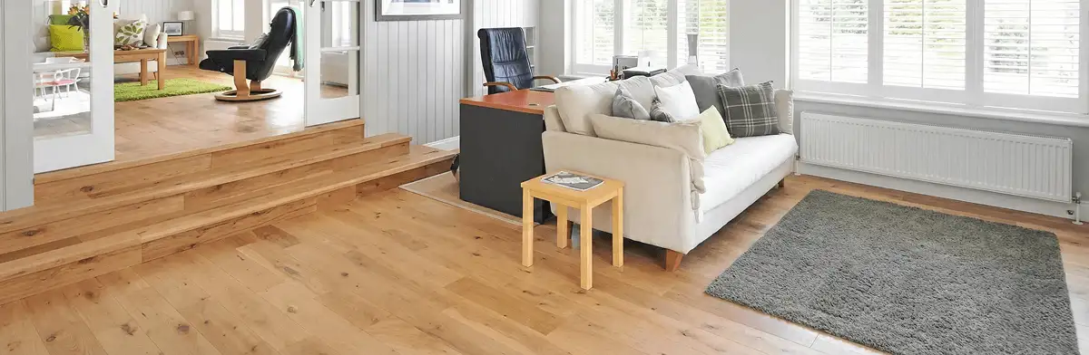 A modern living room with professionally installed laminate flooring, a beige sofa, a small side table, a gray rug, and large windows with white shutters in Buffalo, NY